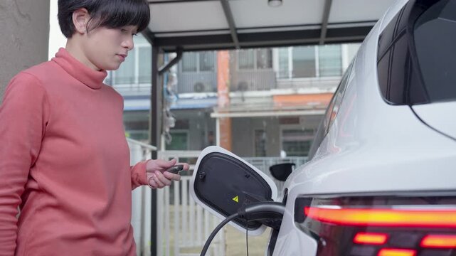 Woman plugs the charging cable of an electric vehicle (EV car), Sustainable clean energy