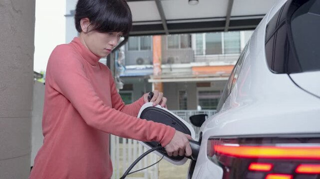 Woman plugs the charging cable of an electric vehicle (EV car), Sustainable clean energy