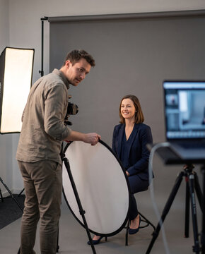 Photographer checks a tethered laptop preview and adjusts a reflector during a corporate headshot studio session