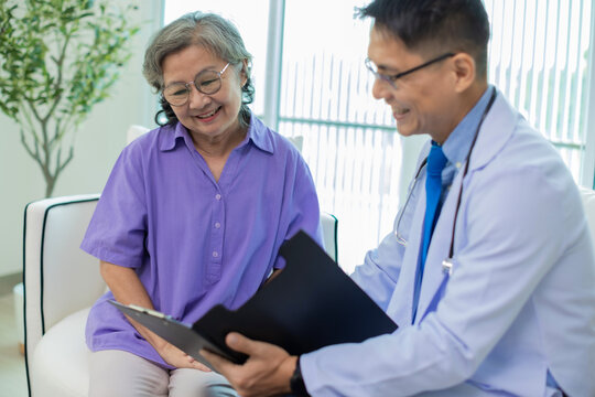 Doctor assisting her old patient at nursing home. Caregiver helping senior patient sit on sofa. Friendly Doctor talking with patient at nursing home