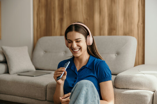 Young woman laughing, enjoying music with headphones at home