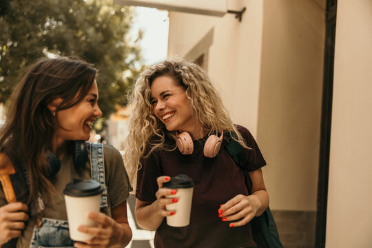 Happy friends walking city street drinking coffee
