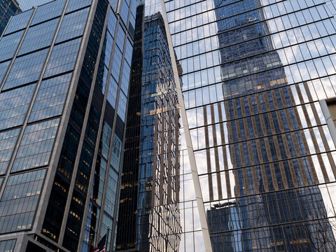 Low-angle view of glass-clad business office towers at Hudson Yards in Manhattan, including one tower with a distinctive rippled, wave-like glass facade. 