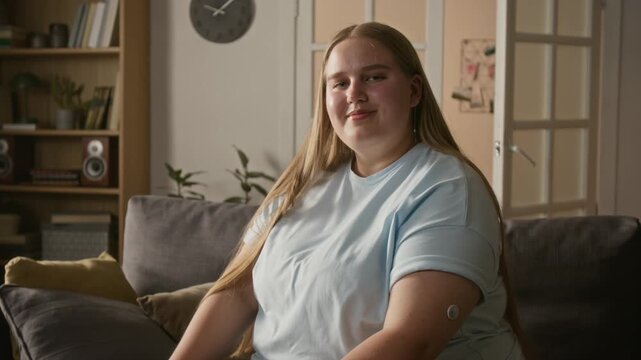 Portrait of smiling Caucasian young adult woman wearing glucose monitoring sensor patch on arm. Useful for diabetes care marketing and medical technology campaigns