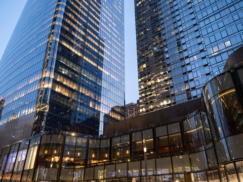 Wide low-angle view of glass-clad business office towers in Midtown Manhattan at dusk, their illuminated interior floors visible through the curtain wall facade.