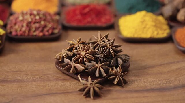 star anise, badian seeds or Illicium verum in a square bowl on a wooden table, surrounded by various spices and herbs.