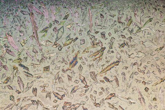 Magnesium sulfate rhomboid and lanceolate crystals under polarized light microscope. Abstract polarized light microscopy background of crystalline mosaic structures on pastel backdrop
