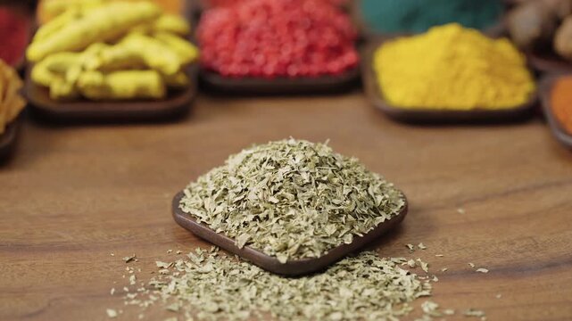 dried parsley leaves flakes petroselinum crispum plant in a square bowl on a wooden table, surrounded by various spices and herbs.
