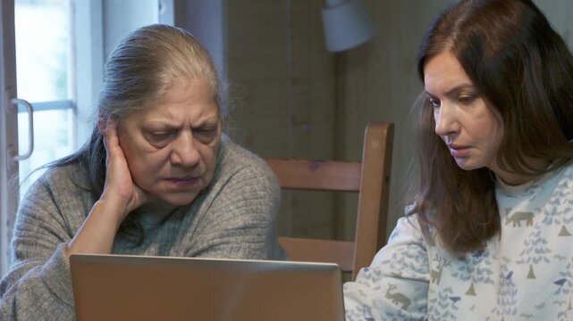 Two women look intently at a laptop screen together indoors. They concentrate seriously on the work. The quiet room feels calm and thoughtful.