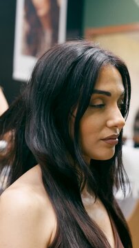 Professional hairstylist using a blow dryer to style a beautiful woman's long, dark hair in a beauty salon. Haircare and styling session. Vertical