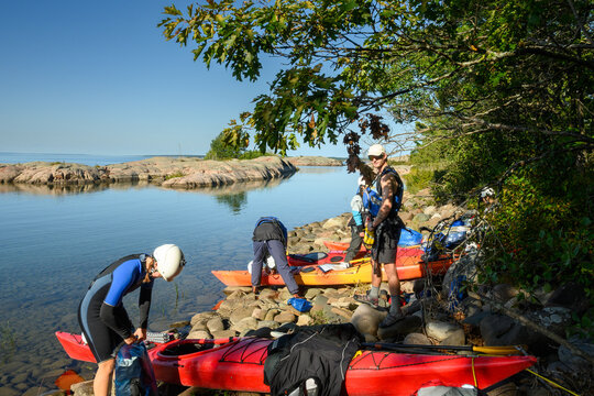 Group of sea kayakers pack kayaks on a rocky island shore under oak trees in morning light on Georgian Bay, Ontario, Canada