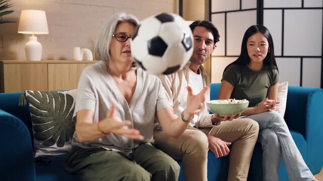 Multi generational family watching a sports match together on a sofa, eating popcorn and supporting their favorite team with excitement