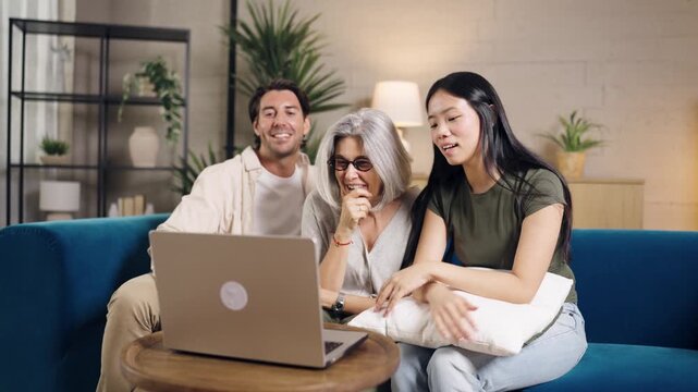 Happy family with an elderly mother, adult son, and daughter in law talking on a video call using a laptop in their living room