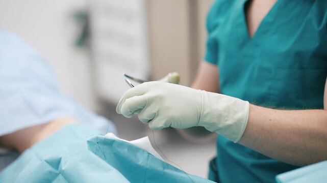 Focused surgeon wearing scrubs and a mask carefully stitching a wound with a needle and thread during a medical procedure in a hospital