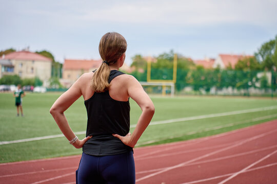 Woman standing with hands on hips by running track before workout