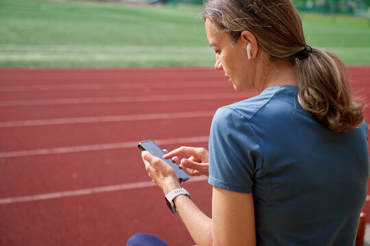 Woman using smartphone, checking her running stats at stadium