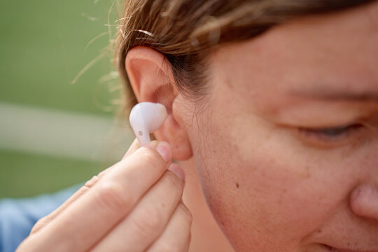 Close-up of a woman pressing a white wireless earbud into her ear outdoors