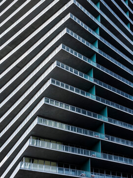 Low angle view of the corner of a high-rise apartment building. Cantilevered concrete balconies with glass railings step outward in diagonal rows.
