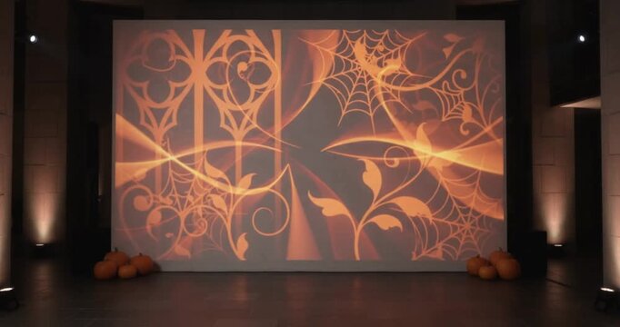 Large indoor projection screen displaying orange gothic decorative patterns, spider webs, and elegant abstract graphics