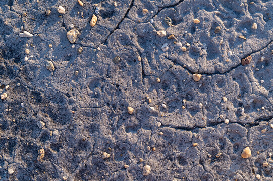 Cracked rough concrete surface covered with sand and small pebbles