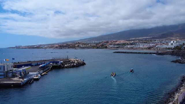 Dron vuela desde el rompeolas de un puerto sobre el oc&eacute;ano Atl&aacute;ntico con peque&ntilde;os barcos y la costa de Costa Adeje al fondo, Tenerife, Islas Canarias