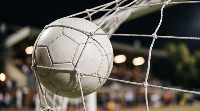 White football caught in goal net with blurred stadium floodlights bokeh background