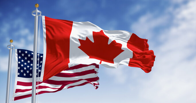 Canada and american national flags waving in the wind on a clear day