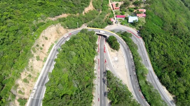 Aerial view drone road in construcction in middle of mountains, curved road cars traveling trees and grass, Colombia 4k