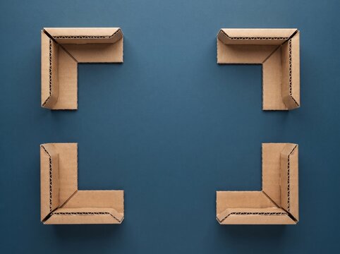 Four corner protective cardboard inserts arranged in a frame shape on a dark blue background for shipping