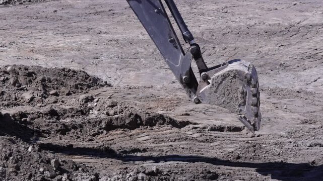 Raw industrial power meets stubborn, saturated soil; thick mud clings to the bucket as the machine wrestles the unyielding terrain