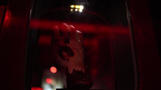 Halloween horror display with a severed hand behind glass under deep red lighting creating a disturbing haunted house atmosphere filled with fear suspense and mystery