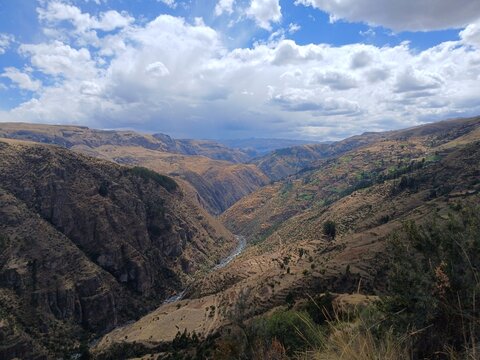 Valley with a distant river, mountains, forest, and a cloudy sky in the background in Surimana, Cusco, Peru.