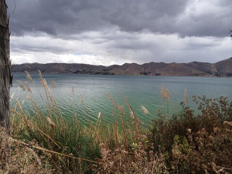 View of a lagoon in the foreground and mountains under a cloudy sky in Mosocllacta, Cusco, Peru.