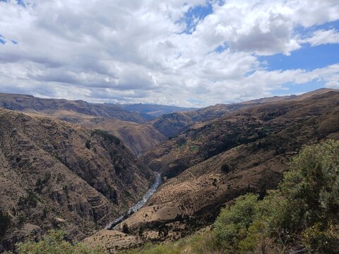 Valley with a distant river, mountains, forest, and a cloudy sky in the background in Surimana, Cusco, Peru.
