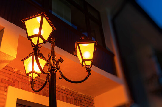 A vintage street lamp illuminates a building exterior with warm yellow light at twilight.