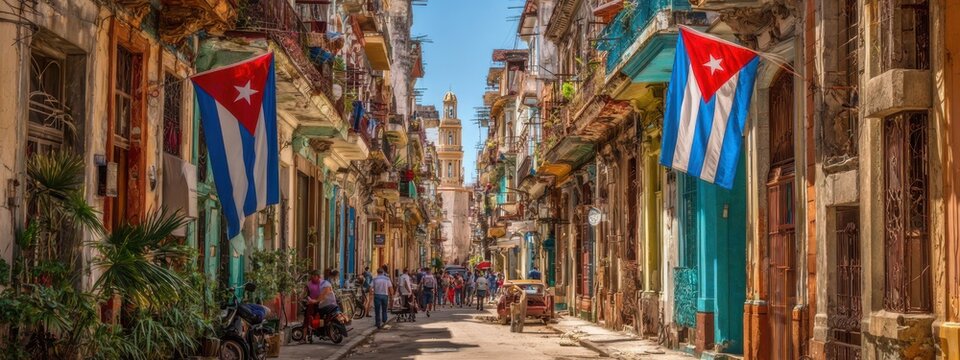 People walk along a street in Havana, Cuba, with Cuban flags hanging from buildings on a sunny day