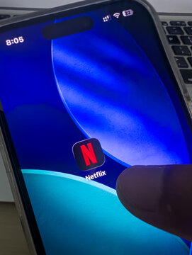Netflix app icon on smartphone screen with finger tapping close up stock photo