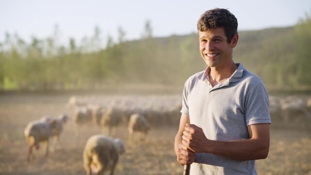 Authentic portrait of a smiling shepherd feeling proud of his job. A herd of sheep is grazing in the background at sunset