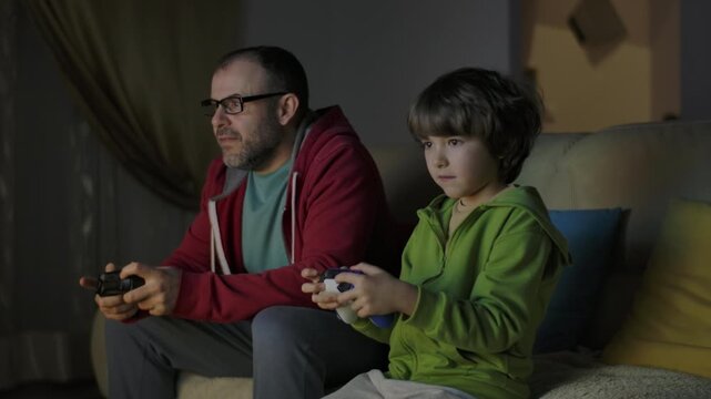 Father and Son Expressing Emotions While Enjoying Relaxing Together, Playing Video Games in Front of TV.  Family Time Hobby. Family Having Fun Together at Home in Living Room Playing Video Games.