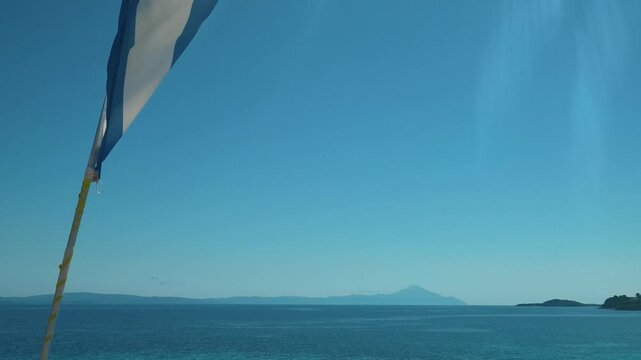 Greece flag flaps in wind against clear sky. Trani Ammouda, Greece