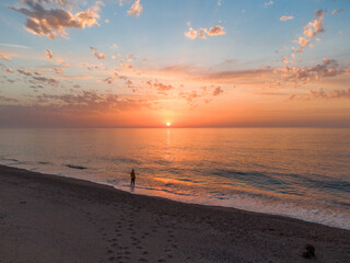 Lonely man relaxing on the beautiful beach at sunset. Sun reflected on beach, Lonely man stands on the beach looks towards the sun light. A man meets the sunset on beach, silhouette of person walking. © Mediterranean sea