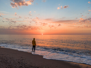 Lonely man relaxing on the beautiful beach at sunset. Sun reflected on beach, Lonely man stands on the beach looks towards the sun light. A man meets the sunset on beach, silhouette of person walking. © Mediterranean sea