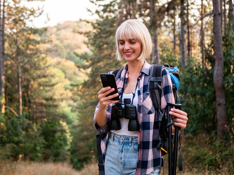Portrait of happy woman hiker using smartphone for map and direction while hiking through forest, enjoying nature, exploration, adventure and active lifestyle.