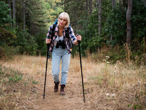 Woman hiker showing exhaustion while hiking in the mountains, resting on a footpath with her backpack and hiking pole during an active outdoor adventure.