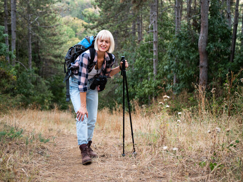 Tired woman hiker holding her painful knee while hiking through wilderness, struggling with a possible sprain or muscle injury.