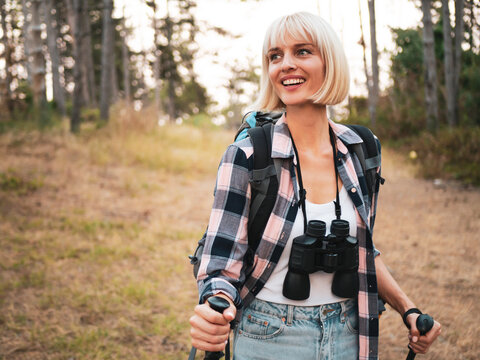 Happy woman hiker on a hiking adventure in the mountains, walking through wilderness with backpack and hiking pole, enjoying freedom, recreation and beautiful nature.