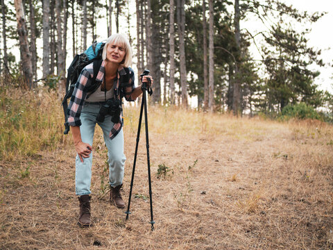 Woman hiker experiencing knee pain while hiking through a forest, resting on footpath and feeling tired and worried after injury.