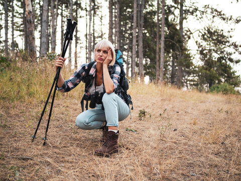 Tired woman hiker hiking in the forest, resting with backpack and hiking pole after difficult walk, showing exhaustion and physical effort.