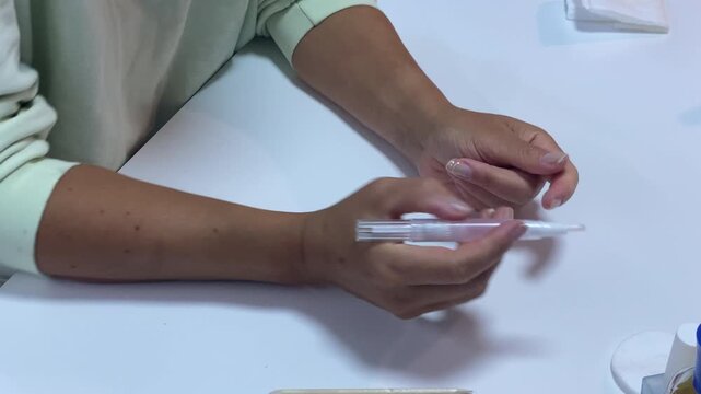 A gentle woman applies nourishing cuticle oil to her nails using a pen applicator. She takes care of her hands at a clean white desk. This cozy routine creates a feeling of peace and calm.