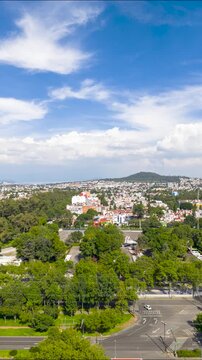 Vertical video with aerial timelapse of clouds forming over Cerro de la Estrella and traffic flowing through a tree-lined intersection in Coyoacan, Mexico City, Mexico